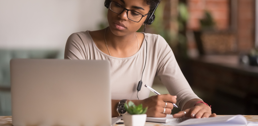 Person looking at laptop and writing notes in notebook