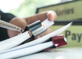 person writing on paper with a payroll folder in the background