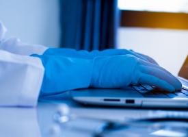 doctor using laptop with vial sitting next to it