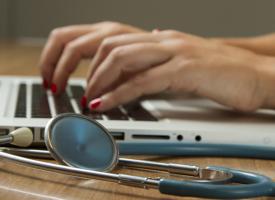person typing on laptop with stethoscope