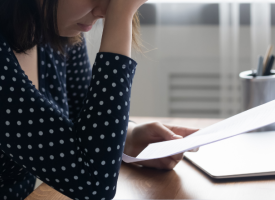 A student weary and stressed head in hands at a desk looking at a sheet of paper 