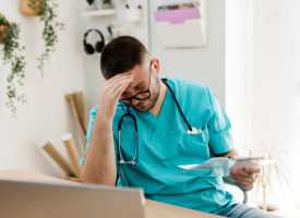 Stressed young male doctor at his desk head in hand 