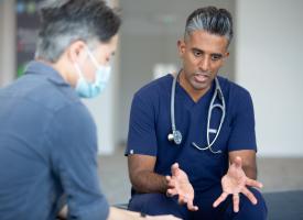 doctor in scrubs explaining something to a patient wearing a surgical mask