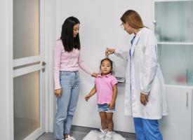 Image of doctor checking small child's height while mother looks on