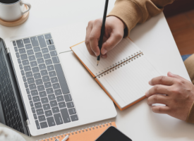 Person taking notes at desk and computer