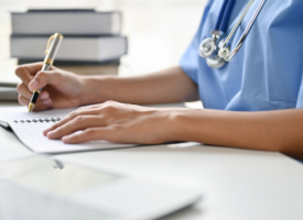 Doctor wearing blue scrubs and a stethoscope completing paper work at a desk