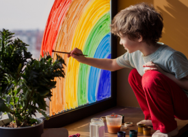 Child painting rainbow on glass window
