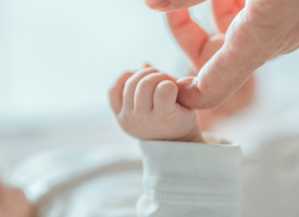 A newborn baby grabs the finger of an adult hand.