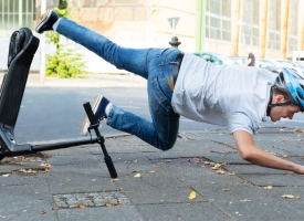 A man wearing a helmet falls off an e-scooter.