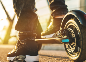The bottom half of two legs astride an e-Scooter.