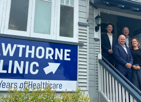 Five people stand at the top of a staircase out the front of a Queenslander building. A sign in front says "Hawthorne Clinic".