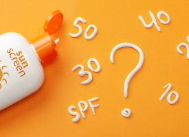A bottle of SPF 50 sunscreen on an orange background. There are numbers written in white sunscreen such as 10, 20, 30, 40 and 50. There is also a question mark.
