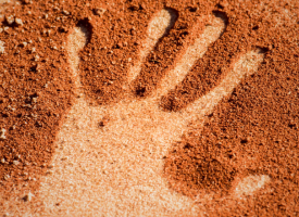 Hand shape on sand, in the style of Indigenous art