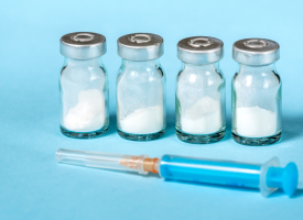 Four vials of powder and a syringe on a blue background