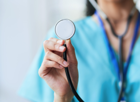 A female doctor in blue scrubs holds up a stethoscope