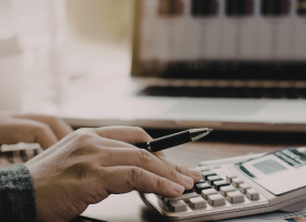Hand using calculator with screen in background