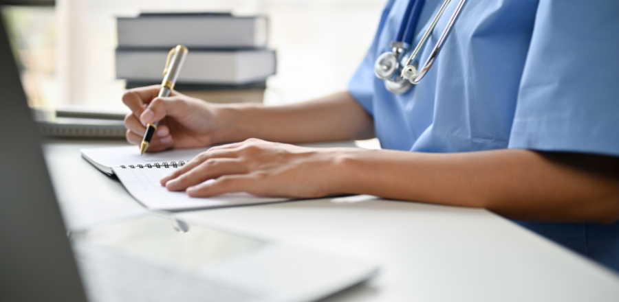 Doctor wearing blue scrubs and a stethoscope completing paper work at a desk