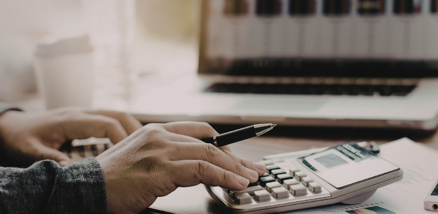 Hand using calculator with screen in background